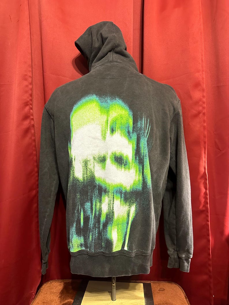 May include: Black hooded sweatshirt with a green and white graphic print of a skull on the back.