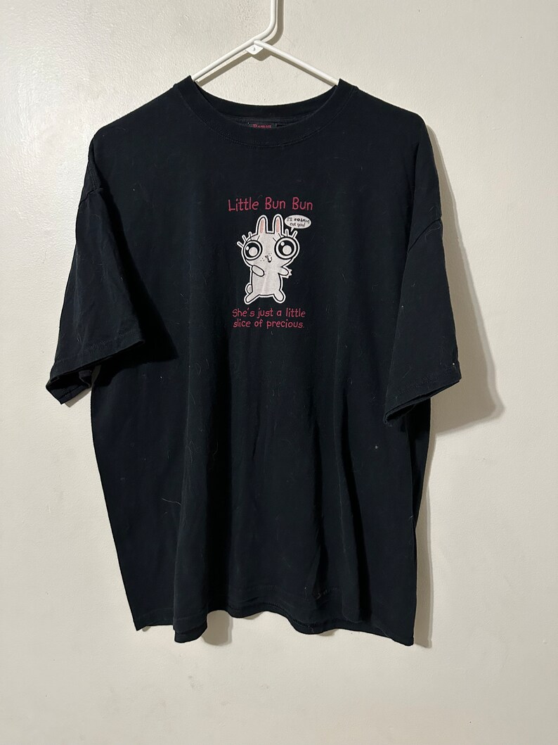 May include: Black t-shirt with a cartoon bunny graphic and the text "Little Bun Bun." The bunny has large eyes and is holding a speech bubble that says "I'm happy 4 you!" The text "She's just a little slice of precious" is below the bunny.