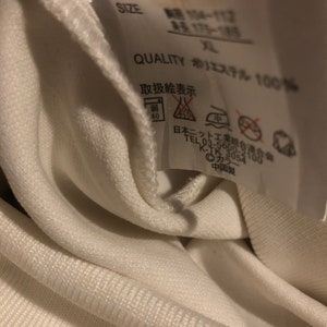 May include: White clothing tag with black text that reads "STYLNO. EV56492", "SIZE", "QUALITY", "エステル 100%", and "取扱絵表示". The tag also includes a washing instruction symbol.