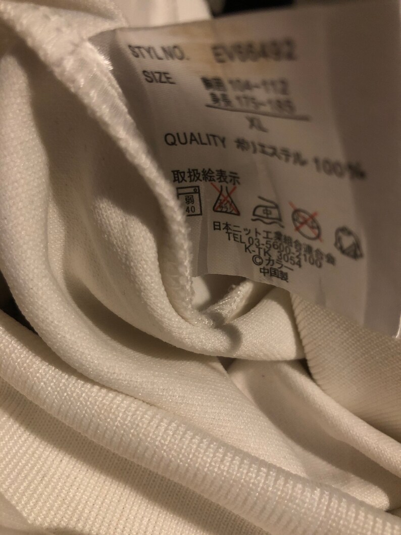 May include: White clothing tag with black text that reads "STYLNO. EV56492", "SIZE", "QUALITY", "エステル 100%", and "取扱絵表示". The tag also includes a washing instruction symbol.