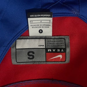 May include: A gray and white tag with the text "TEAM ENGINEERED TO THE NAME/# EXACT SPECIFICATIONS OF CHAMPIONSHIP ATHLETES" and a Nike swoosh logo. The tag also has the text "S" in a larger font.