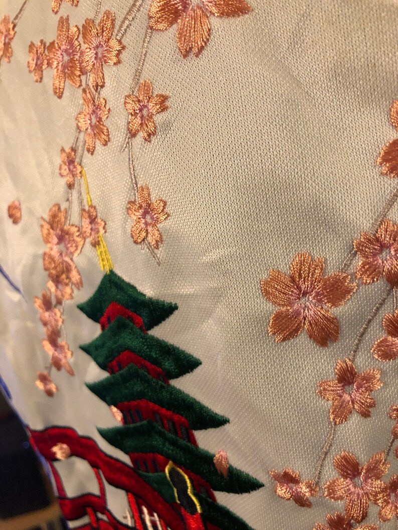 May include: White fabric with embroidered pink cherry blossoms and a red and green pagoda.