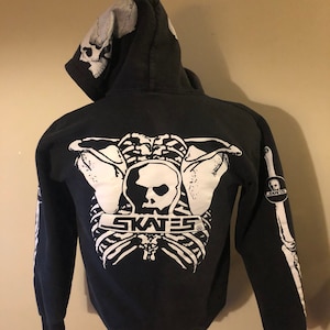 May include: Black zip-up hoodie with a white skeleton graphic on the back. The graphic includes the text "SKATES" and a skull. The hoodie has a white skull graphic on the hood.
