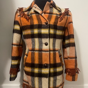 May include: A long-sleeved plaid jacket with brown, orange, white, and black plaid pattern. The jacket has fringe trim on the shoulders, cuffs, and hem.