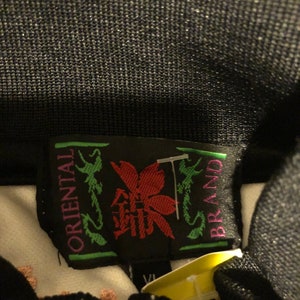 May include: A black and green label with white text that reads "Oriental Brand". The label features a red flower with a green stem and leaves. The label is attached to a white garment.