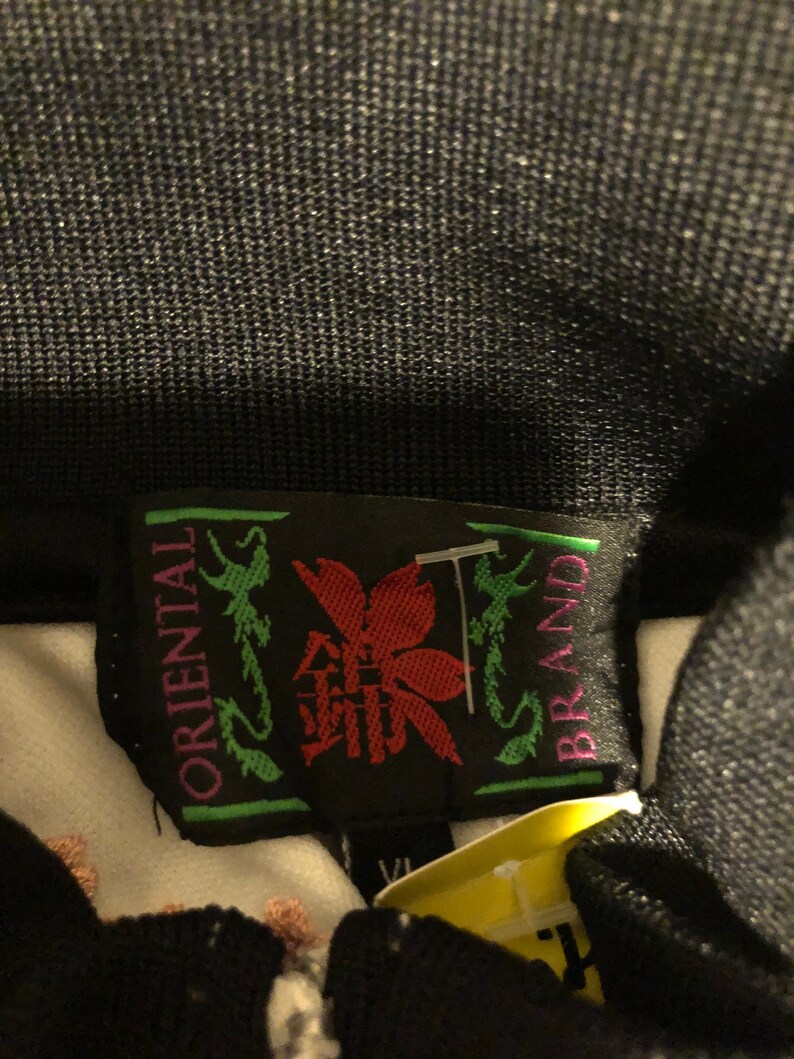 May include: A black and green label with white text that reads "Oriental Brand". The label features a red flower with a green stem and leaves. The label is attached to a white garment.