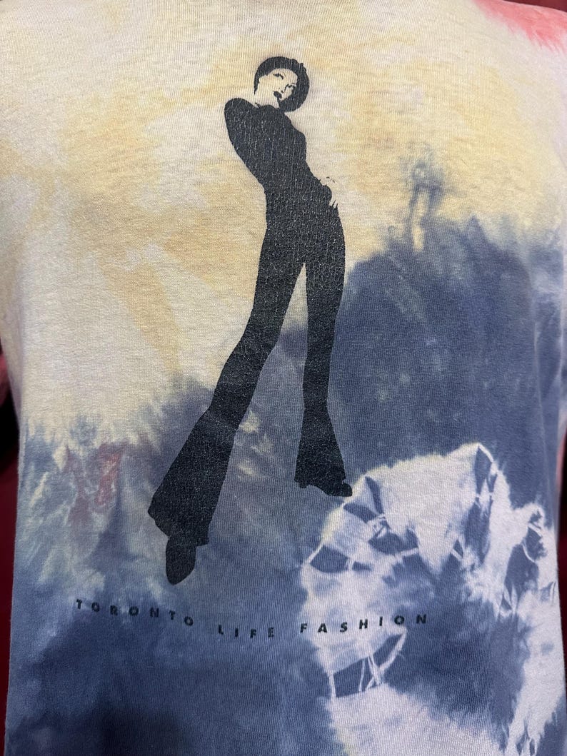 K&ouml;nnte beinhalten: Ein Batik-T-Shirt mit einer schwarzen Silhouette einer Frau in einer stilvollen Pose. Das Shirt tr&auml;gt den Text "Toronto Life Fashion" auf der Unterseite.