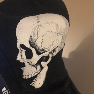 May include: Black hooded sweatshirt with a white skull graphic on the front. The skull is a detailed anatomical illustration. The text "SKATES" is visible on the bottom left corner of the sweatshirt.