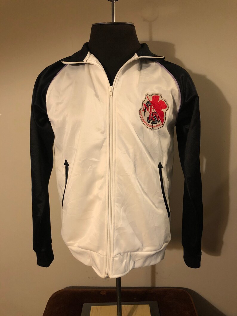 May include: White and black track jacket with a zipper closure. The jacket has a purple stripe on the collar and a red and black embroidered patch on the chest. The patch features a scorpion and the text "Scorpions Wrestling Federation".
