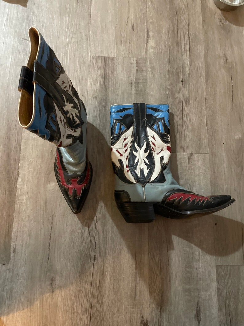 May include: A pair of cowboy boots with a black, white, blue, and red design. The boots have a pointed toe and a high heel.