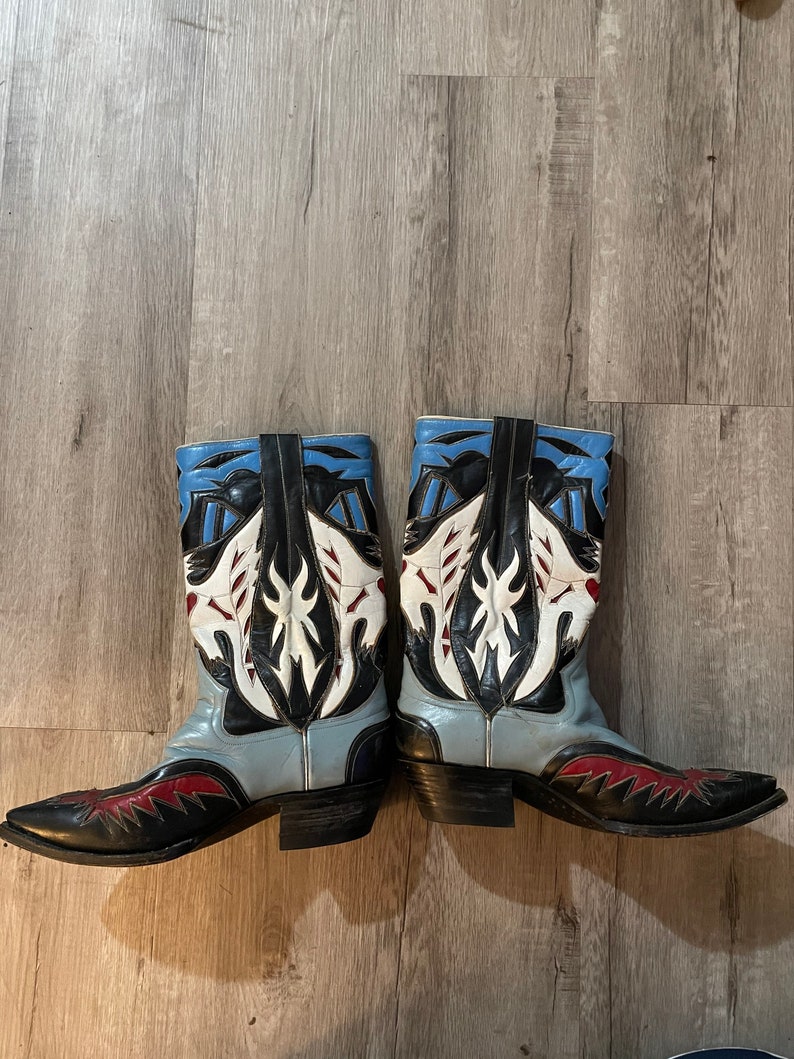 May include: A pair of blue, black, white, and red cowboy boots with intricate designs on the shaft.