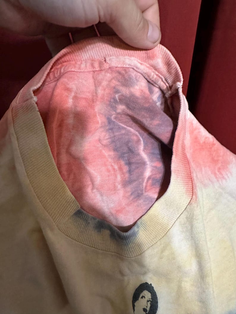 K&ouml;nnte beinhalten: Ein Batik-T-Shirt mit einem verblassten Farbverlauf in Rosa, Gelb und Blau. Das Shirt hat einen Rundhalsausschnitt und eine lockere Passform.