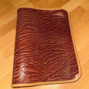 May include: A brown leather portfolio with a textured surface and a tan trim.