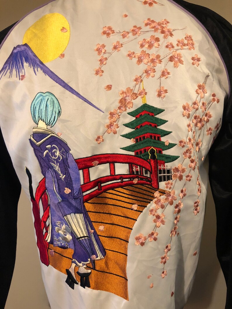 May include: A white satin bomber jacket with an embroidered design of a woman in a blue kimono walking across a red bridge. The bridge is over a river with a green pagoda in the background. The design also includes a mountain and a yellow moon. The jacket has black sleeves.