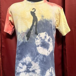K&ouml;nnte beinhalten: Ein Batik-T-Shirt mit einer Silhouette einer Frau in einem langen Rock und dem Text "Taking Life Fashion" auf der Vorderseite.