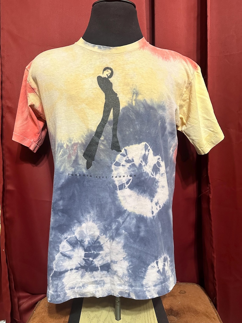K&ouml;nnte beinhalten: Ein Batik-T-Shirt mit einer Silhouette einer Frau in einem langen Rock und dem Text "Taking Life Fashion" auf der Vorderseite.