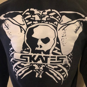 May include: Black hoodie with a white graphic of a skeleton holding a skull with the word "SKATES" printed below.