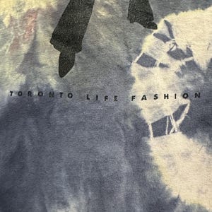 K&ouml;nnte beinhalten: Ein blaues Batik-T-Shirt mit einer schwarzen Silhouette einer Person, die Schlaghosen tr&auml;gt, und dem Text "Toronto Life Fashion" unten.