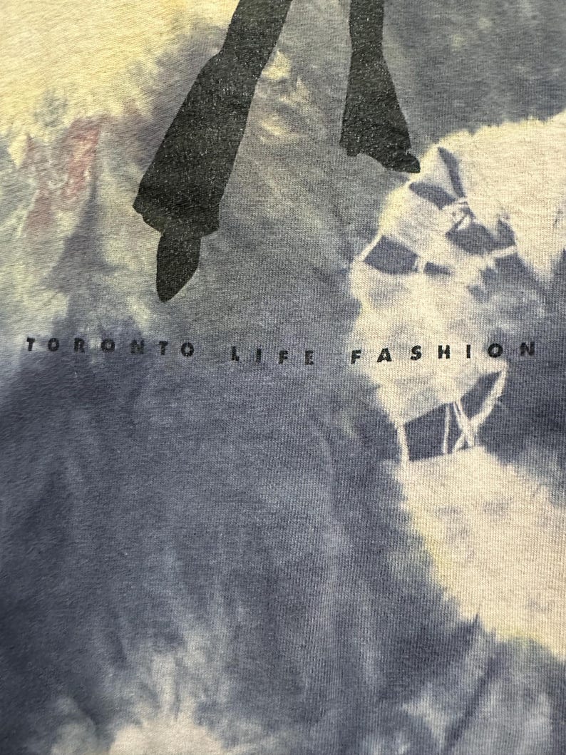 K&ouml;nnte beinhalten: Ein blaues Batik-T-Shirt mit einer schwarzen Silhouette einer Person, die Schlaghosen tr&auml;gt, und dem Text "Toronto Life Fashion" unten.