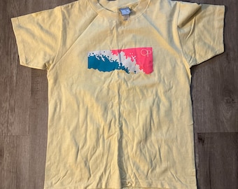 May include: A yellow t-shirt with a blue, pink, and white graphic design. The graphic features a stylized wave design with the letters "OP" in pink.