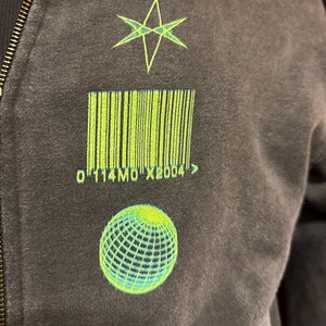 May include: A black zip-up hoodie with a green star, barcode, and globe graphic. The barcode has the text "0114M0X2004" below it.