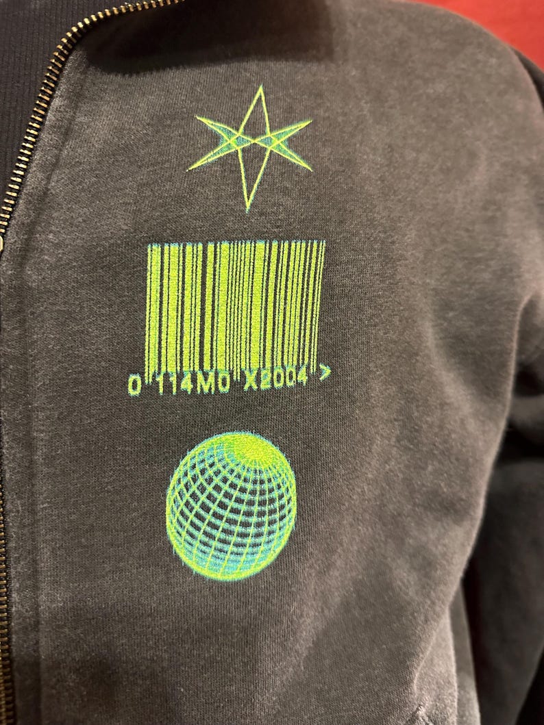 May include: A black zip-up hoodie with a green star, barcode, and globe graphic. The barcode has the text "0114M0X2004" below it.