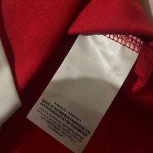 May include: A white tag with black text on a red background. The tag reads "Made in Indonesia/Fabrique en Indonesie/Hecho en Indonesia", "100% Polyester/Polyester/Poliester", "Exclusive of Decoration/Decoration Non Comprise/No Incluye La Decoracion", "RN#56323/CA#05553".