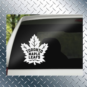 May include: White vinyl decal of the Toronto Maple Leafs logo on a car window. The logo features a stylized maple leaf with the words "Toronto Maple Leafs" inside.