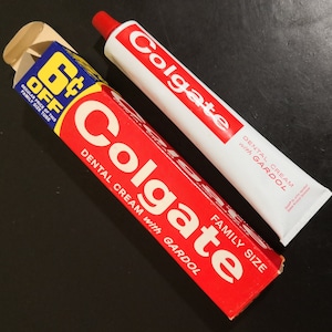 May include: A red and white Colgate toothpaste tube with the text "DENTAL CREAM with GARDOL" and a red and white Colgate toothpaste box with the text "DENTAL CREAM with GARDOL" and "FAMILY SIZE". The box has a blue and white 6¢ OFF sticker.