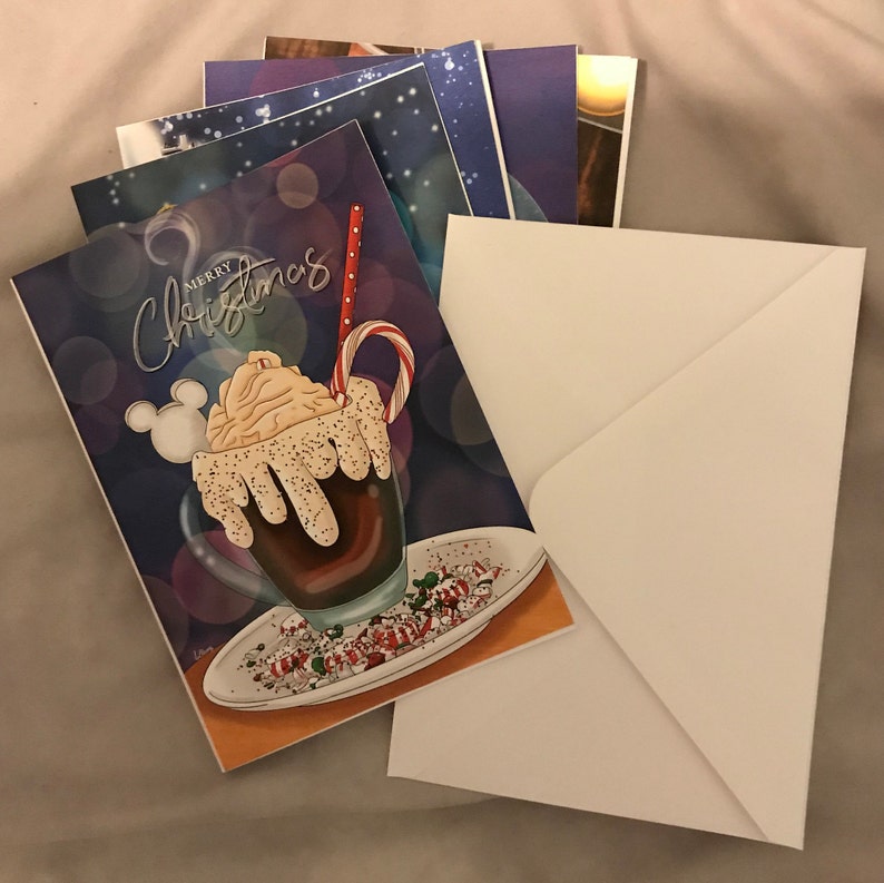 May include: A Christmas card with a festive design featuring a hot chocolate drink topped with whipped cream and sprinkles. The card says "Merry Christmas" in a whimsical font.