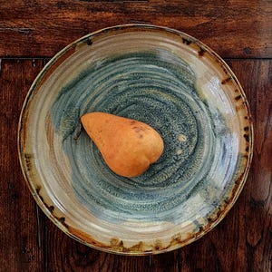 May include: A single orange pear sits on a blue and brown ceramic plate with a swirl pattern. The plate has a light brown rim.