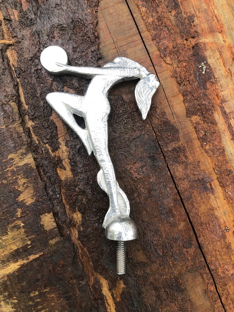 Op de afbeelding: Zilverkleurige metalen sculptuur van een vrouw die een bol vasthoudt. Het beeld is bevestigd aan een schroefdraadstang.
