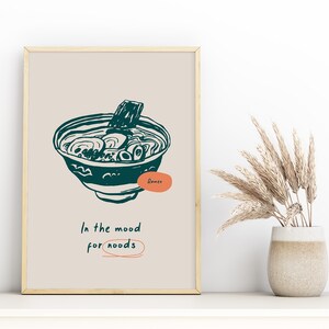 May include: A beige poster with a teal illustration of a bowl of ramen noodles. The text "Ramen" is written in a teal circle. The text "In the mood for noodles" is written in black with a teal circle around the word "noodles".