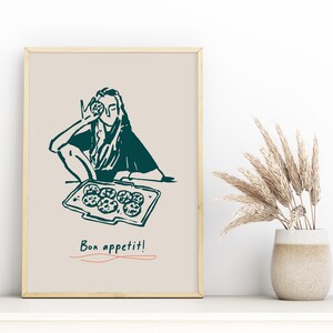 May include: A framed illustration of a person holding a cookie and a tray of cookies with the text "Bon appetit!" in a teal color.