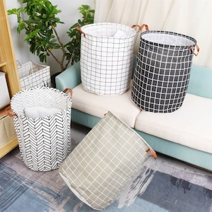May include: Four fabric storage bins with different geometric patterns. The bins are black and white checkered, gray and white checkered, white and black chevron, and beige and white checkered. The bins are on a light blue couch and a gray rug.