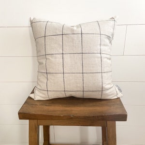 May include: A cream-colored pillow with a black and white checkered pattern. The pillow is sitting on a wooden stool.