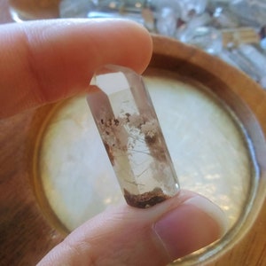 May include: A clear quartz crystal point with brown and grey inclusions. The crystal is faceted and has a pointed tip.