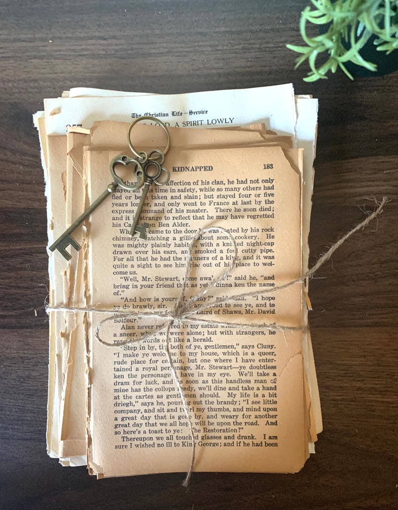 May include: A stack of vintage paperback books tied together with twine and a decorative key. The books are yellowed with age and have a worn, well-loved look. The key is a skeleton key with a heart-shaped bow.