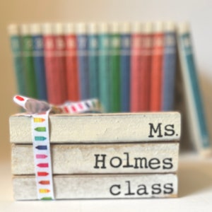 May include: A stack of three white wooden blocks with black text that reads "Ms. Holmes class". The blocks are decorated with a colorful ribbon with a crayon pattern.
