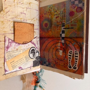 May include: Open journal with mixed media art. The left page has a pocket with a vintage postcard and a dictionary page with a gramophone illustration. The right page features colorful abstract art with circles, spirals, and checkered patterns. The journal is bound with a brown spine.