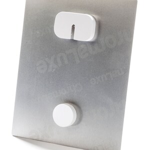 May include: Back of a metal print with a brushed silver finish. The back features two white mounting components for hanging. Text at the top reads "Back of Metal Print." The bottom text says "Wall mount included for easy hanging off the wall."