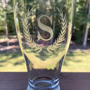 May include: A clear glass beer mug with a white etched design of a wreath with the letter "S" in the centre.