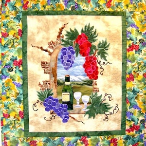May include: A quilted wall hanging with a green border and a central image of a brick archway with a view of a vineyard and mountains. The archway is adorned with purple and red grapes, green leaves, and a bottle of wine with two wine glasses.