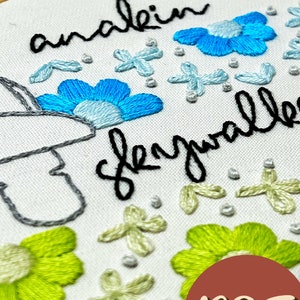 May include: Embroidered hoop art with the text "analein slayalle" in black cursive. The hoop features blue and green flowers, and white and light green floral designs.