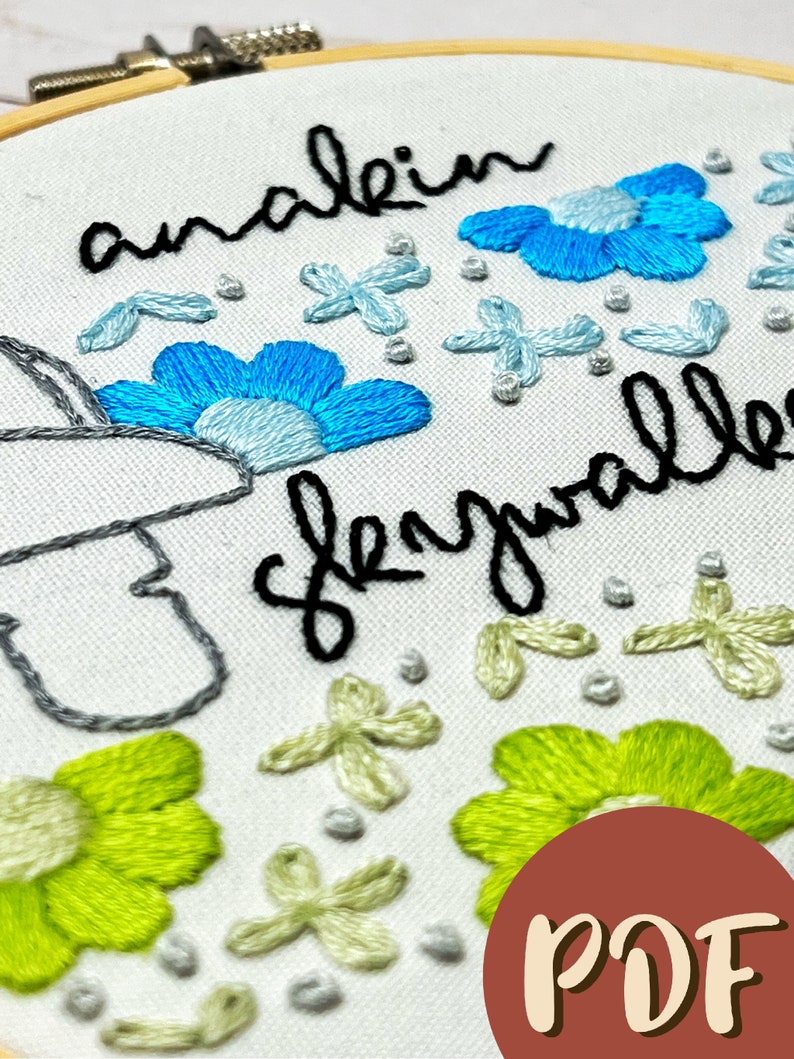 May include: Embroidered hoop art with the text "analein slayalle" in black cursive. The hoop features blue and green flowers, and white and light green floral designs.