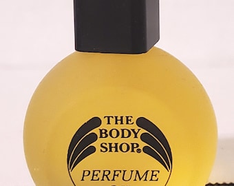 May include: A yellow glass bottle with a black cap and a black label that reads "THE BODY SHOP" and "PERFUME OIL".