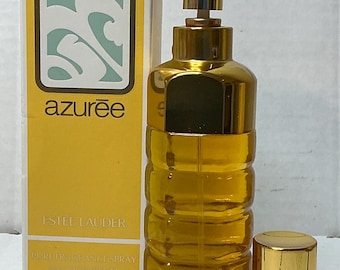 May include: A gold-toned perfume bottle and matching cap next to a yellow box. The bottle is cylindrical with a ribbed design and contains a golden liquid. The box features the word "azurée" and the brand name "ESTEE LAUDER".