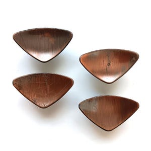 May include: Four copper-toned, triangular-shaped cabinet knobs with a slightly curved, rounded edge.