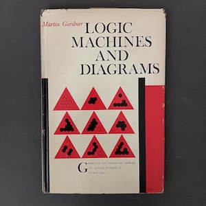 Puede incluir: Un libro blanco con una encuadernación roja y negra. El título es "Logic Machines and Diagrams" de Martin Gardner. La portada presenta un diseño geométrico de triángulos rojos con formas negras en su interior.