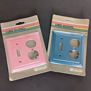 Puede incluir: Dos tapas de tomacorriente, una rosa y otra azul, con las palabras "color accents" impresas en el embalaje. Ambas tapas tienen un solo interruptor de luz y una toma de corriente doble.